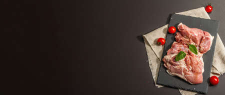 Raw turkey thigh with spices. Fresh boneless meat on a ceramic stand. Modern hard light, dark shadow. Black stone concrete backgroundの写真素材