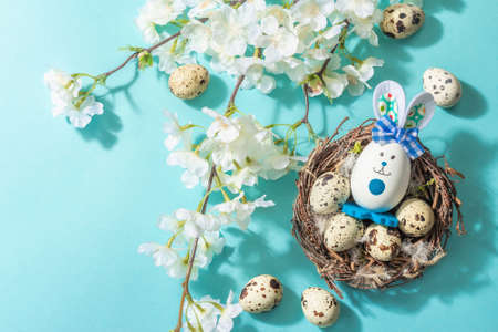 Happy Easter blue background with blooming cherry, quail eggs in a nest and cute rabbit. Spring flat festive lay, traditional symbols, hard light dark shadow, top viewの写真素材
