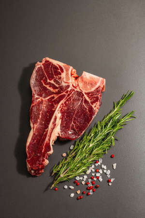 Classic T-bone steak with spices on a black stone concrete background. Fresh rosemary, trendy hard light, dark shadow, flat lay, top viewの写真素材