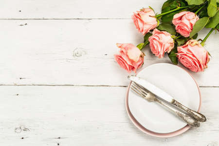 Romantic dinner table on white wooden background. Love concept for Valentine's or Mother's day, Wedding cutlery. Bouquet of fresh pink roses, table setting, top viewの写真素材