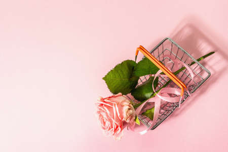 Sale concept with a shopping basket and fresh rose. Zero-waste, trendy hard light, dark shadow, flat lay. Women, Valentine's or Mother's Day, Wedding. Delicate pink background, top viewの写真素材