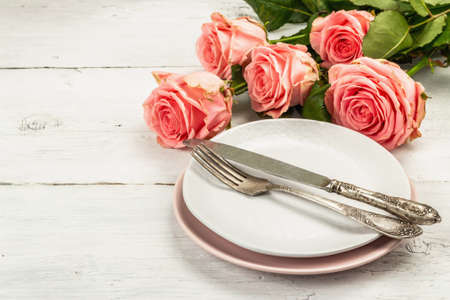 Romantic dinner table on white wooden background. Love concept for Valentine's or Mother's day, Wedding cutlery. Bouquet of fresh pink roses, table setting, copy spaceの写真素材