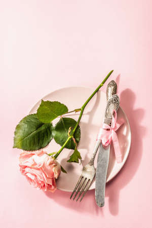 Romantic dinner table isolated on rose background. Love concept for Valentine's or Mother's day, Wedding cutlery. A delicate fresh pink rose, table settingの写真素材