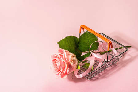 Sale concept with a shopping basket and fresh rose. Zero-waste, trendy hard light, dark shadow, flat lay. Women, Valentine's or Mother's Day, Wedding. Delicate pink background, copy spaceの写真素材