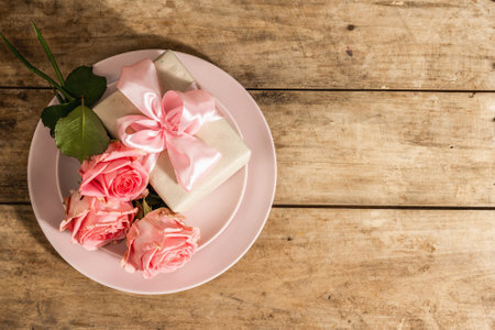 Romantic dinner table on wooden rustic background. Love concept for Valentine's or Mother's day, Wedding cutlery. Delicate fresh pink roses, gift, vintage table setting, top viewの写真素材