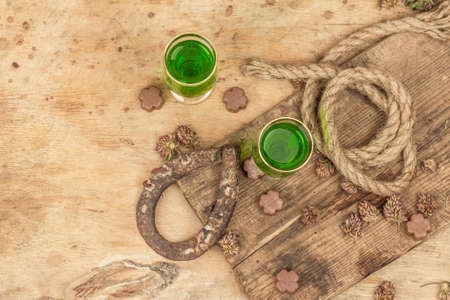 St. Patrick's Day concept. Traditional green cocktail, sweet chocolate in the shape of clover leaves, horseshoe, vintage rope. Traditional decor, wooden background, top viewの写真素材