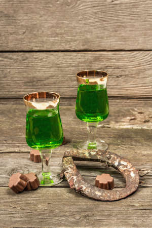 St. Patrick's Day concept. Traditional green cocktail, sweet chocolate in the shape of clover leaves, horseshoe, vintage rope. Traditional festive decor, wooden background, copy spaceの写真素材