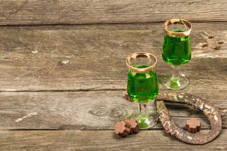 St. Patrick's Day concept. Traditional green cocktail, sweet chocolate in the shape of clover leaves, horseshoe, vintage rope. Traditional festive decor, wooden background, copy spaceの写真素材