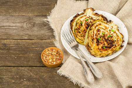 Homemade vegan cabbage steaks with herbs and spices. Healthy food ready to eat on a serving plate, cutlery. Old wooden background, copy spaceの写真素材