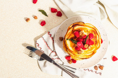 Classic homemade American pancakes with frozen raspberries, hazelnut and mint. Healthy breakfast, cutlery, light stone concrete background. Trendy hard light, dark shadow, top viewの写真素材