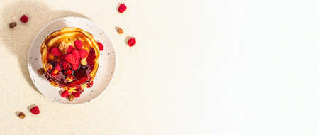 Classic homemade American pancakes with frozen raspberries, hazelnut and mint. Healthy breakfast on light stone concrete background. Trendy hard light, dark shadow, banner formatの写真素材