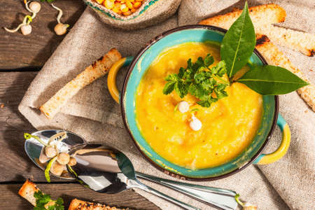 Pea cream soup in a bowl on vintage wooden background. Dry legumes, toast, croutons and greens. Delicious vegan healthy food. A trendy hard light, dark shadow, rustic style, top viewの写真素材