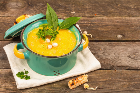 Pea cream soup in a bowl on vintage wooden background. Dry legumes, toast, croutons and greens. Delicious vegan healthy food. A trendy hard light, dark shadow, rustic style, copy spaceの写真素材