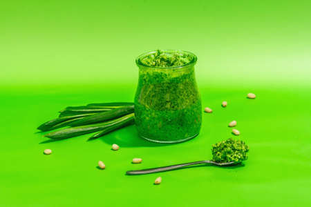 Wild leek pesto with olive oil, parmesan, and pine nuts isolated on bright green background. Fragrant dip in a glass jar. A hard light, dark shadow, copy spaceの写真素材