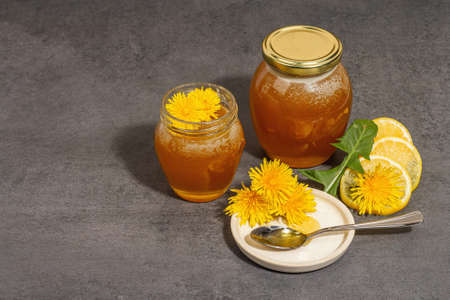 Dandelion jam or honey in the glass jar with fresh blooming dandelion flowers. Seasonal product, trendy hard light, dark shadow. Stone concrete background, copy spaceの写真素材