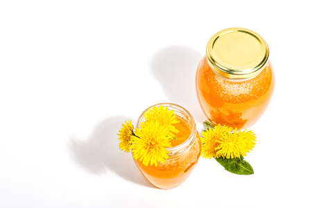 Dandelion jam or honey in the glass jar with fresh dandelion flowers isolated on white background. Seasonal product, trendy hard light, dark shadow, top viewの写真素材