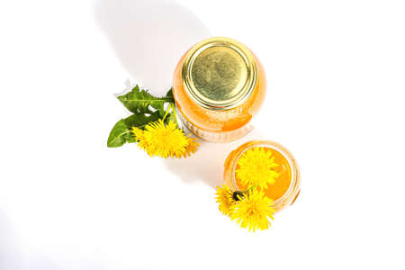 Dandelion jam or honey in the glass jar with fresh dandelion flowers isolated on white background. Seasonal product, trendy hard light, dark shadow, top viewの写真素材