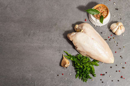 Raw chicken breast with spices and fresh parsley. Farm product, BIO poultry. Healthy food concept, trendy hard light, dark shadow. Gray concrete stone background, top viewの写真素材
