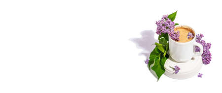 Cup of coffee and lilac flowers bouquet isolated on a white background. Breakfast springtime concept, trendy stand. A hard light, dark shadow, banner formatの写真素材