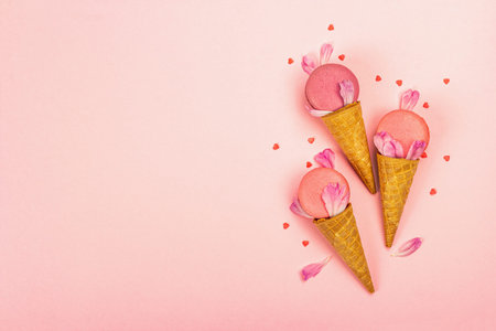 Ice cream waffle cones with macarons on pink background. Sweet dessert, colorful and pastel candy...