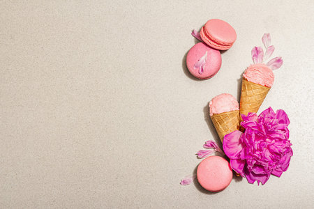 Ice cream waffle cones with macarons on a stone background. Sweet dessert, peonies flower petals,...