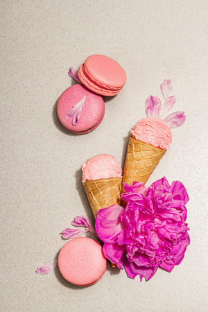 Ice cream waffle cones with macarons on a stone background. Sweet dessert, peonies flower petals,...