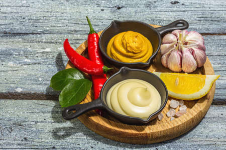 Mustard and mayonnaise sauces. Fresh mint, lemon, garlic, and spices. A hard light, dark shadow, wooden boards background, flat lay, copy spaceの写真素材