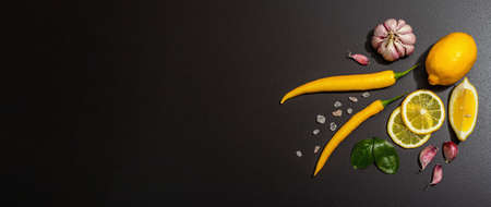 Cooking ingredients background. Spices, vegetables, garlic, yellow peppers chili. Black background, preparation food concept, flat lay, hard light, dark shadow, banner formatの写真素材