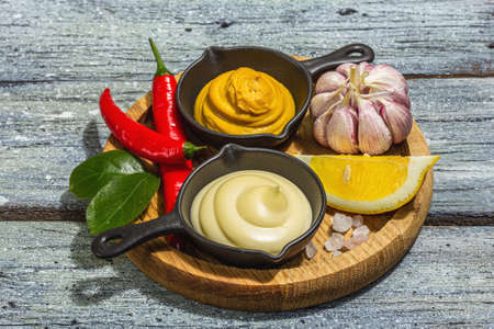 Mustard and mayonnaise sauces. Fresh mint, lemon, garlic, and spices. A hard light, dark shadow, wooden boards background, flat lay, close upの写真素材