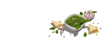 Pesto sauce in a bowl with pine nuts, parmesan and garlic isolated on white background. Trendy hard light, dark shadow, banner formatの写真素材