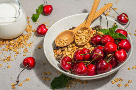 Summer breakfast concept. Healthy morning food. Ripe cherry and granola, light concrete background, flat lay. Trendy hard light, dark shadow, close upの写真素材