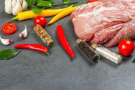 Raw pork loin meat with spices and vegetables on gray stone background. Traditional animal protein for cooking healthy food, fresh tomato and bay leaf. Culinary concrete concept, copy spaceの写真素材
