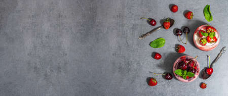 Delicious Italian dessert panna cotta with sweet cherry sauce, fresh strawberries and mint leaves. Stone concrete background, banner formatの写真素材