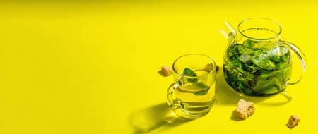 Fresh mint tea in a glass teapot. Brown sugar, healthy breakfast concept. A trendy hard light, dark shadow, bright yellow background, banner formatの写真素材