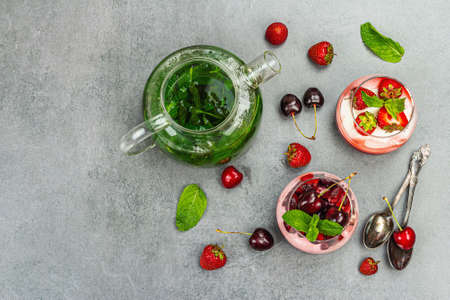 Delicious Italian dessert panna cotta with sweet cherry sauce, and strawberry jam. Mint leaves tea and fresh berries. Stone concrete background, top viewの写真素材