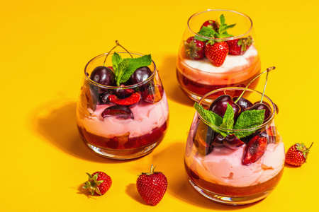 Delicious Italian dessert panna cotta with sweet cherry sauce, strawberry jam, fresh berries and mint leaves. Trendy hard light, dark shadow, bright orange background, close upの写真素材