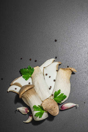 Fresh Pleurotus eryngii mushrooms on black stone concrete background. Spices and herbs, trendy hard light, dark shadow, flat lay, top viewの写真素材