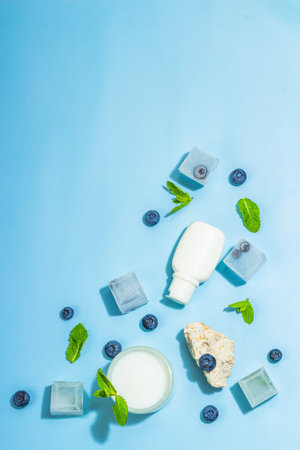 natural skincare. Cream or lotion with organic berries. Blueberry, mint, and ice. Moisturizing and tonic cosmetics concept, flat lay, trendy hard light, dark shadow, blue background, top viewの写真素材