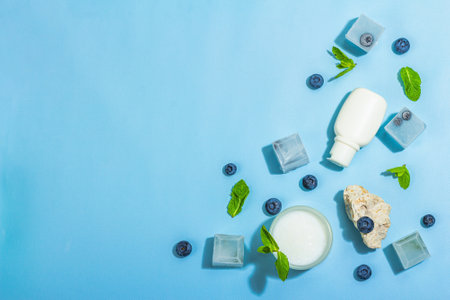 natural skincare. Cream or lotion with organic berries. Blueberry, mint, and ice. Moisturizing and tonic cosmetics concept, flat lay, trendy hard light, dark shadow, blue background, top viewの写真素材