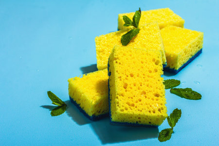Bright yellow sponges for washing dishes. Organic cleaning concept, minty freshness. A trendy hard light, dark shadow, blue background, flat lay, copy spaceの写真素材