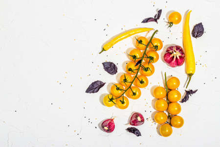 Culinary background with ripe vegetables. Yellow tomato cherries, chili pepper, garlic, purple basil. Fresh vegetables on white putty background, modern hard light, dark shadow, flat lay, top viewの写真素材