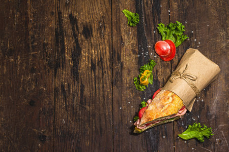 Panini sandwich with ham, crispy salad and vegetables. Healthy food to go concept, lunch or snack option. Trendy hard light, dark shadow, wooden background, top viewの写真素材