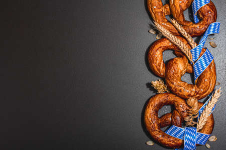 Oktoberfest concept - pretzels with traditional pattern ribbon and ears of wheat. A trendy hard light, dark shadow, black stone concrete background, flat lay, top viewの写真素材