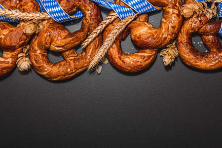 Oktoberfest concept - pretzels with traditional pattern ribbon and ears of wheat. A trendy hard light, dark shadow, black stone concrete background, flat lay, top viewの写真素材