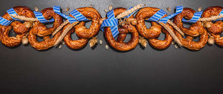 Oktoberfest concept - pretzels with traditional pattern ribbon and ears of wheat. A trendy hard...