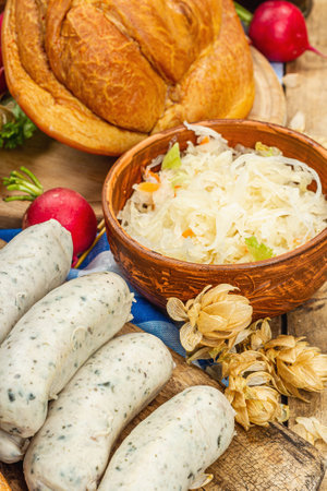 Traditional Oktoberfest set. Pretzels, beer, weisswurst, smoked pork knuckle eisbein with fermented cabbage and mustard. German festival food concept. Old wooden background, close upの写真素材