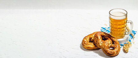 Traditional Oktoberfest set. Pretzels, beer, traditional pattern napkin. German festival food concept. Trendy hard light, dark shadow, white putty background, banner formatの写真素材