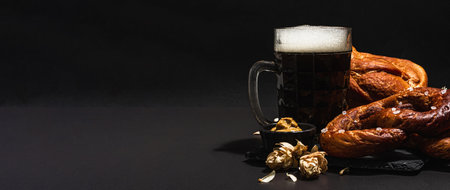 Traditional Oktoberfest set. Pretzels, beer, smoked pork knuckle eisbein with mustard. German festival food concept. Trendy hard light, dark shadow, black stone concrete background, banner formatの写真素材