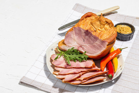 Sliced Oktoberfest smoked pork knuckle eisbein with mustard and chili pepper. Traditional German festival food. Trendy hard light, dark shadow, white plaster background, copy spaceの写真素材