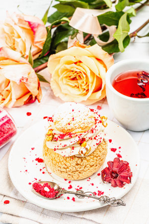 The concept of romantic tea. French Shu cake, hibiscus tea, bouquet of roses, festive decor....